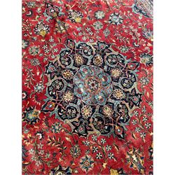 Persian Kashan crimson ground carpet, central rosette medallion on a field of trailing foliate branches decorated with palmettes, scrolling border with repeating plant motifs and flower heads, enclosed within floral pattern guard stripes