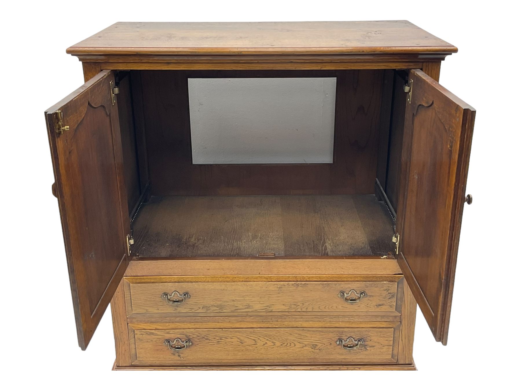 Oak drinks or media cabinet, projecting moulded cornice over two Gothic arch panelled doors on sliding tracks enclosing open storage, two drawers with brass drop handles, on bracket supports