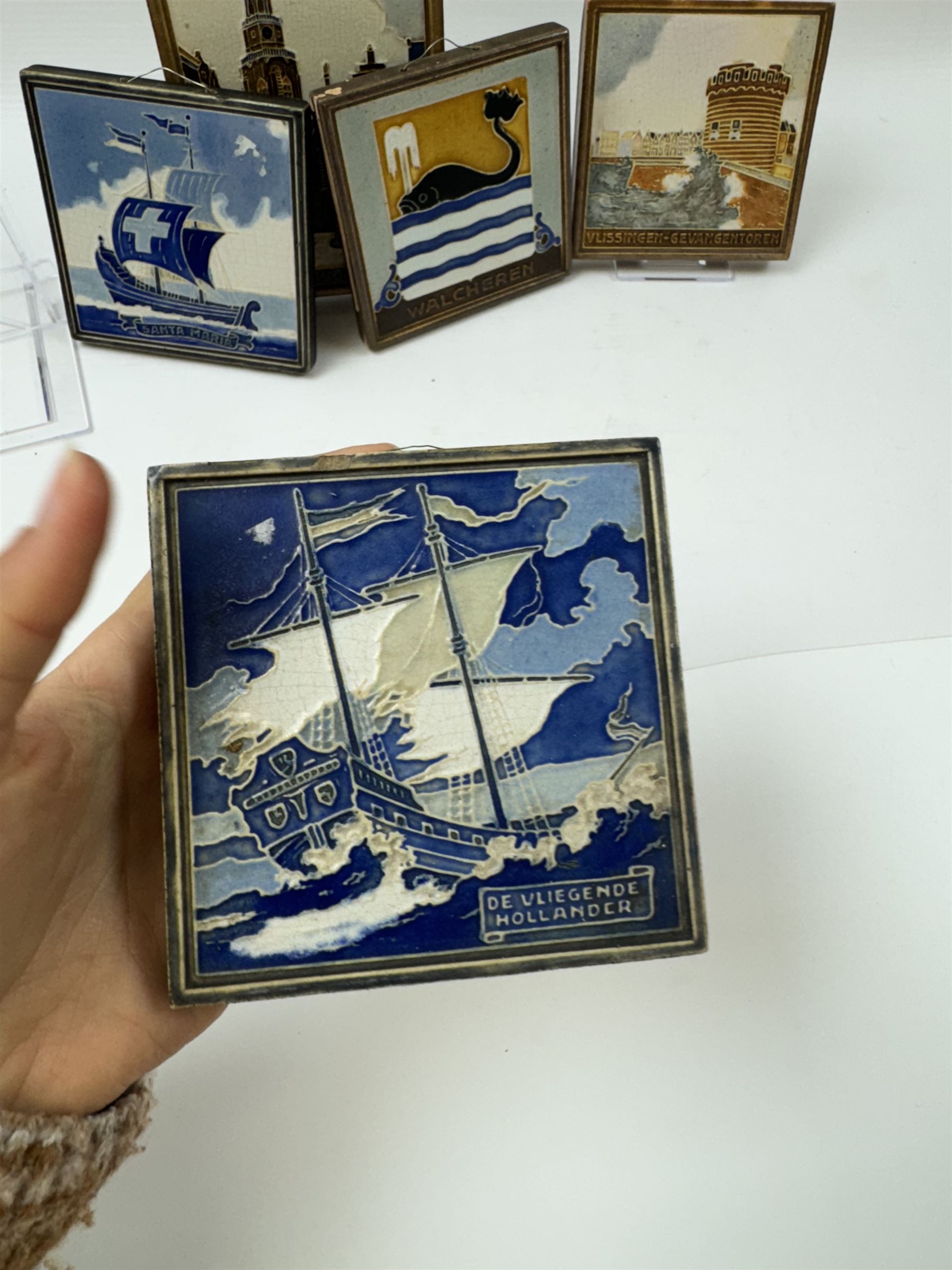 Five Dutch Westraven tiles, to include four square examples depicting maritime and similar scenes, and a rectangular example depicting a village scene, square tiles 10cm x 10cm, rectangular tile 15cm x 10cm