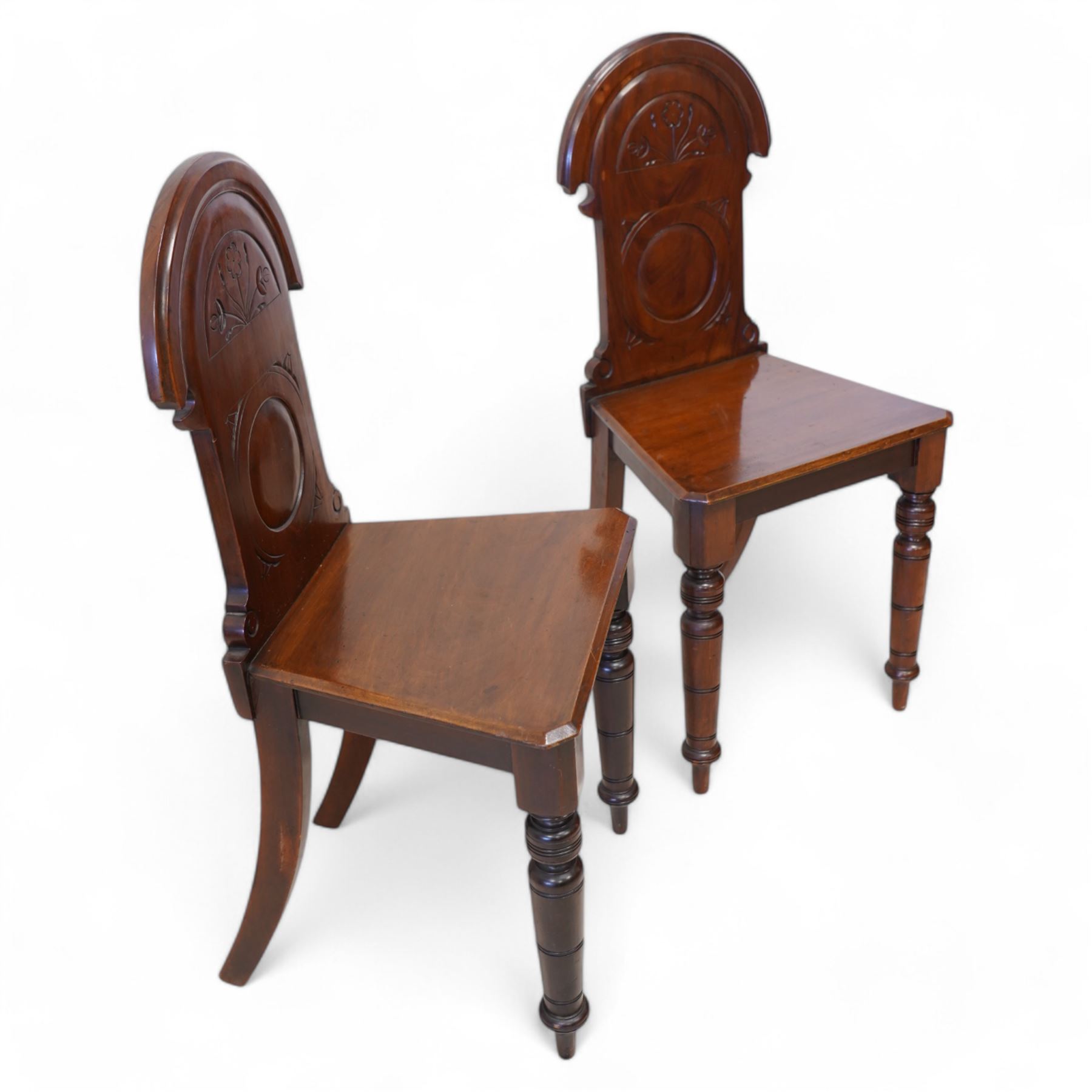 Pair of late Victorian mahogany hall chairs, arched cresting over foliate carved decoration and carved roundel back, chamfered seat over ring turned front supports 