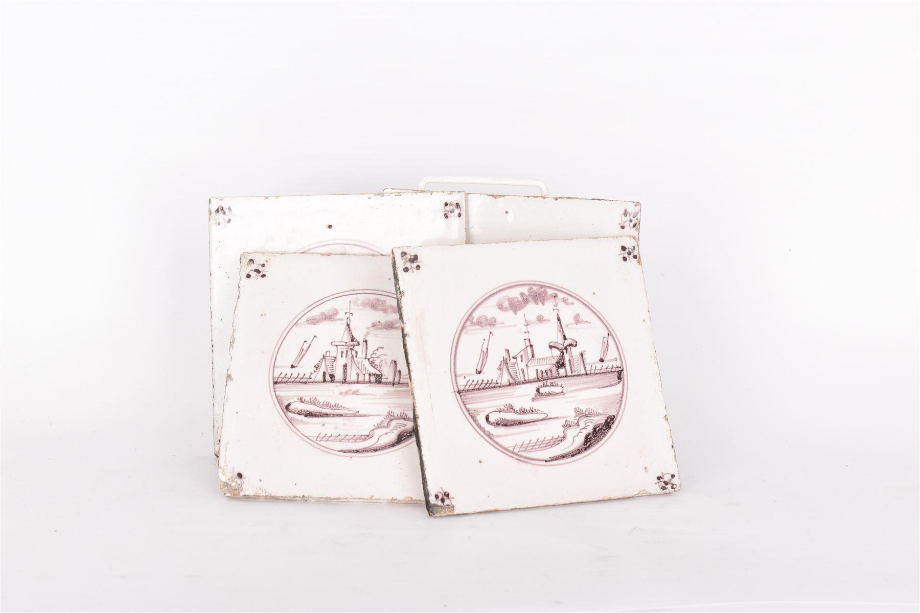 Four Dutch Delft manganese tiles, each depicting a river scene to the centre with a flower to each corner, each tile 12.5cm x 12.5cm