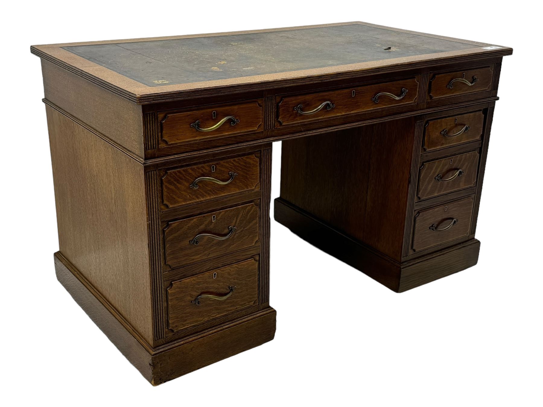 20th century oak twin pedestal desk, rectangular top with inset leather writing surface, fitted with nine drawers with chamfered edges to the raised panels, each with curved brass handles with scroll ends and keyholes, fluted detailing to the top and between the drawers, on moulded plinth base with castors