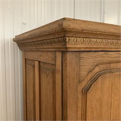 Late 19th century oak triple wardrobe, wide central bevelled mirror door, flanked by two panelled doors each carved with scrolling leaves and flower heads, on moulded skirt base 