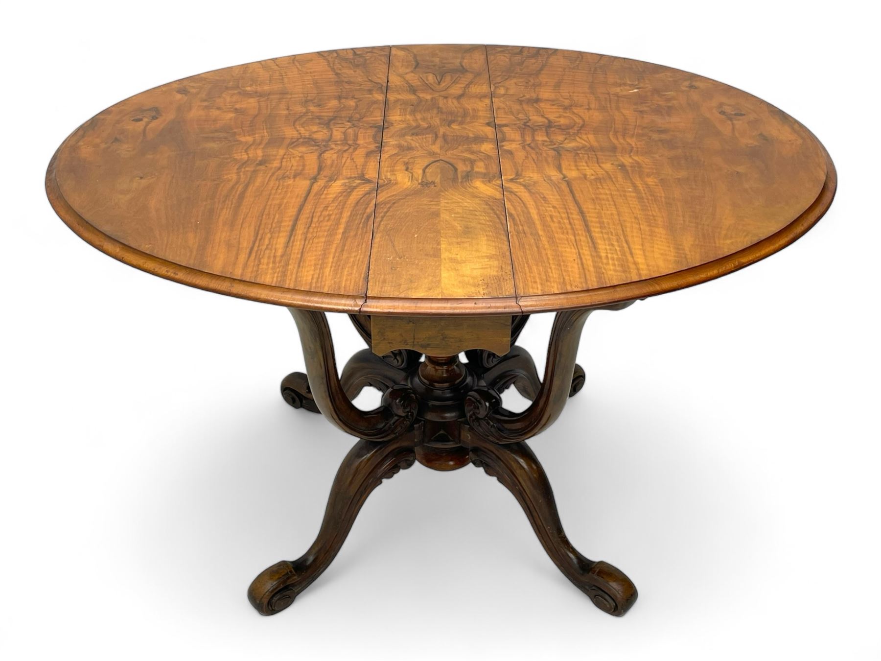 Unusual Victorian figured walnut drop-leaf Sutherland table, moulded drop-leaf oval top, central turned baluster column with quadruple moulded S-scroll supports carved with acanthus leaves, four out-splayed supports with scroll carved terminals, double gate-leg action base, on castors