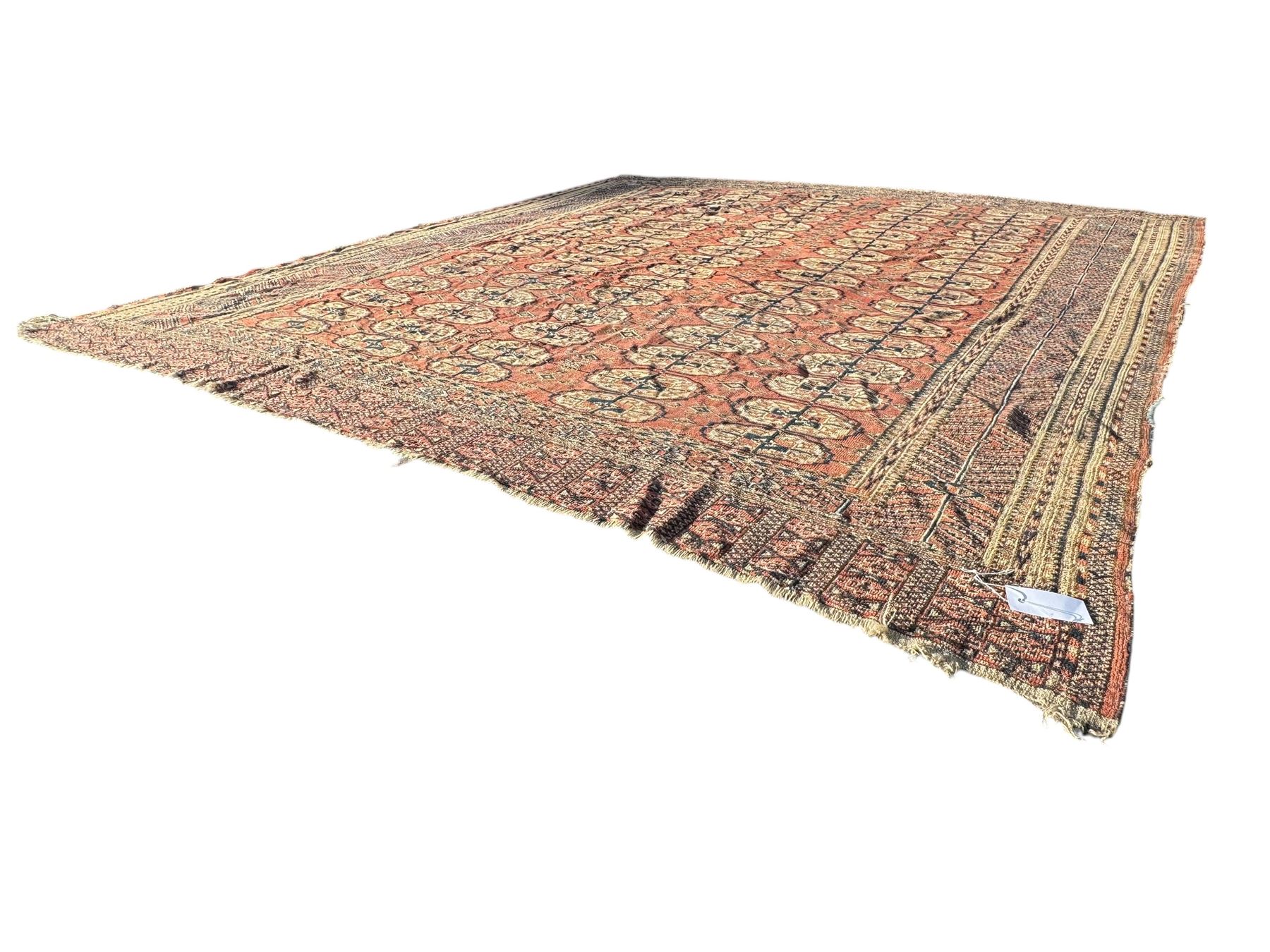 Bokhara red ground carpet, the central field featuring a repeating pattern of traditional octagonal guls arranged in vertical rows, bordered by multiple guard bands with geometric designs, finished with fringed ends