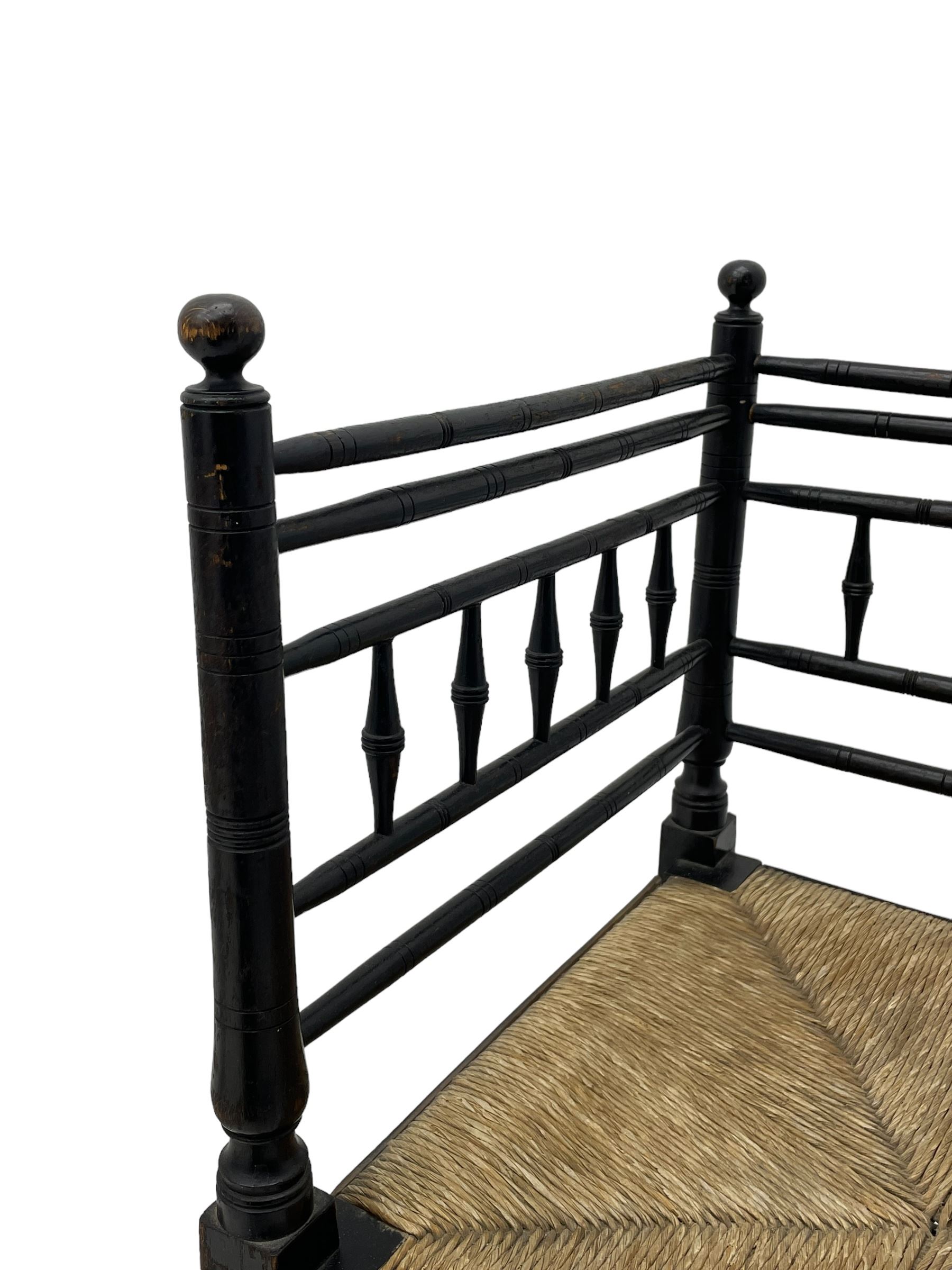 In the manner of William Morris - Arts & Crafts period corner chair, swell turned horizontal rails with balustrade back, rush seat on ring turned supports, black paint finish 