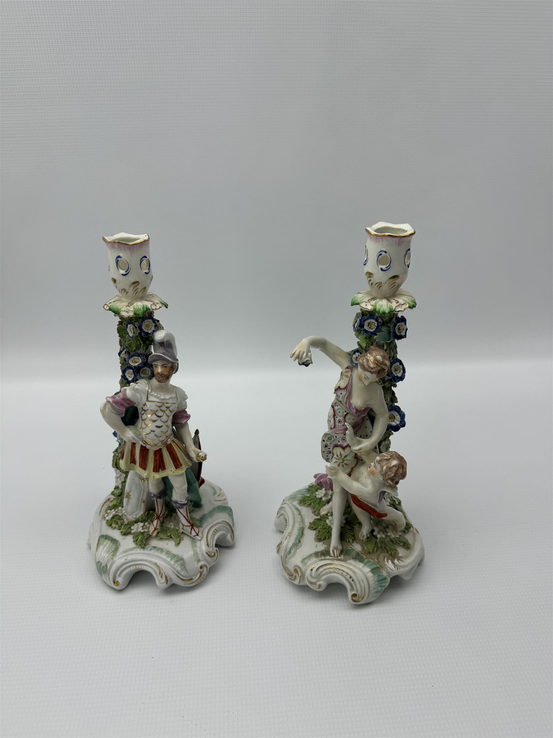 Pair of Derby figural candlesticks, modelled as Venus & Cupid and Mars, Mars wears armour with a shield to his right, Venus dressed in a robe with floral decoration and Cupid by her side, both with pierced sconces above bocage stems, on scrolling raised bases, unmarked, H27cm max (2)