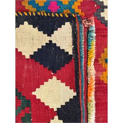 Southwest Persian Qashqai Kilim red ground rug, the central field adorned with rows of multicolored hexagonal medallions with geometric patterns, the border featuring alternating black and white stepped diamonds, narrow band to one end decorated with multicoloured geometric figures