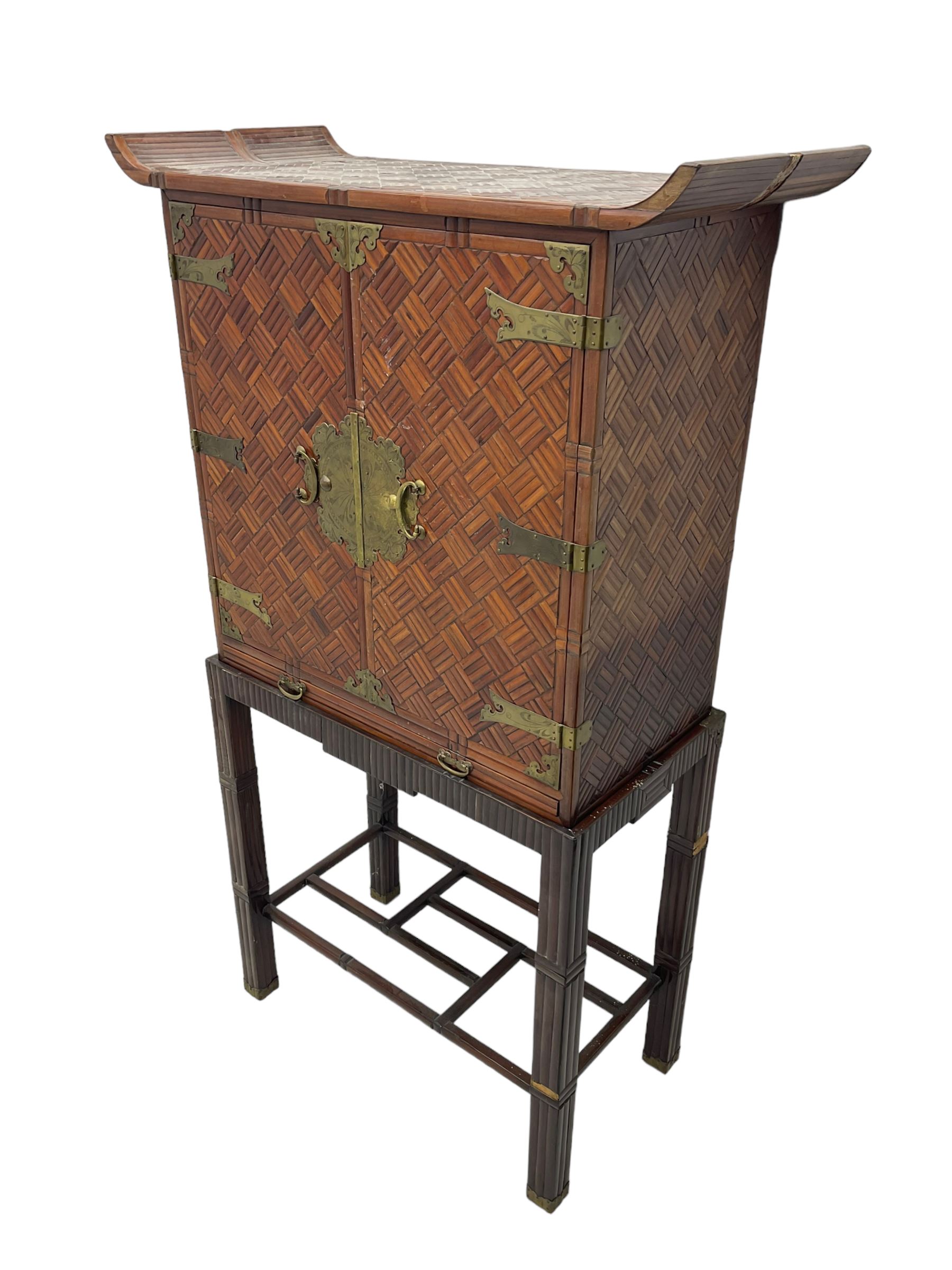 Chinese design bamboo and wood altar cabinet on stand, parquetry lattice-work bamboo, two doors with engraved metal fixtures enclosing drawers and shelf, fitted with slide, the stand pm square supports joined by a series of geometric stretchers