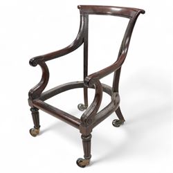 Possibly Gillows - Regency mahogany library chair frame, curved and rolled cresting rail over sweeping arms with lappet and scroll carved terminals, on turned and reed carved supports, brass cups and spoked wheel castors 