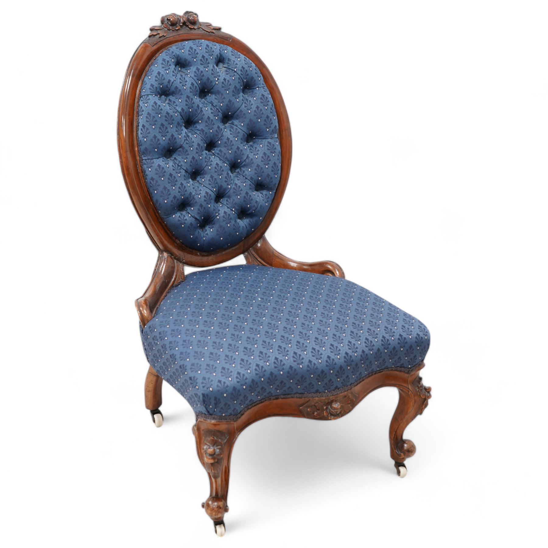 Victorian carved walnut framed nursing chair, the cresting carved with flower heads and extending foliage, upholstered in buttoned blue fabric with repeating pattern, on floral carved cabriole feet