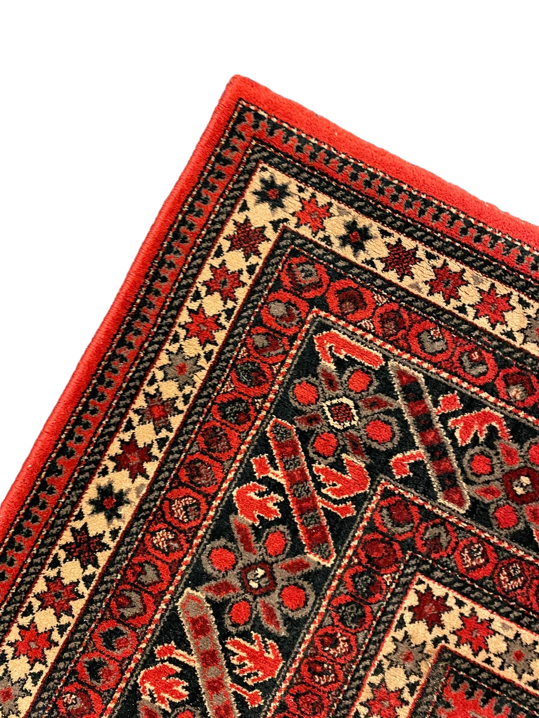 Persian design red ground rug, the field decorated with geometric motifs, repeating multiple band border 