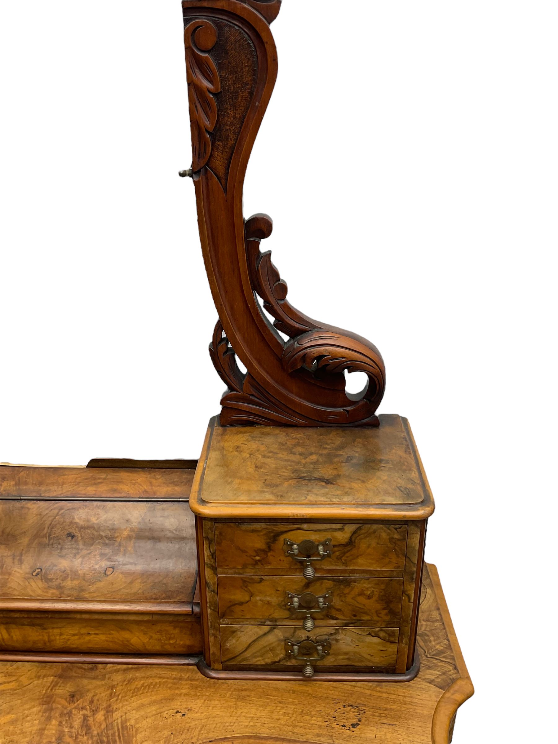 19th century figured walnut dressing table, the raised bevelled mirror back in carved foliage frame with scrolled terminals, fitted with central hinged compartment flanked by small trinket drawers, serpentine moulded top over single frieze drawer, on cabriole supports united by a platform base