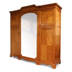 Waring & Gillow Ltd. - Edwardian inlaid satinwood triple wardrobe, stepped moulded cornice over foliate carved edge, single bevelled mirror glazed door enclosing hanging rail and three drawers, flanking panelled doors enclosing hanging rails and hooks, the door frames and panels inlaid with geometric stringing in ebony and satinwood lozenges, reeded and foliate cast loop handles and foliage cast handle plate escutcheon, quarter-matched veneers, on shaped bracket base, the locks stamped 'Gillows Lancaster' and the right hand door with metal marker's plaque 