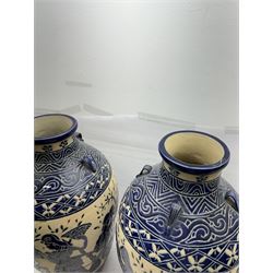 Pair of blue and white Cretan style vases, decorated with figures among trees with blue boarders on a white ground, H55cm