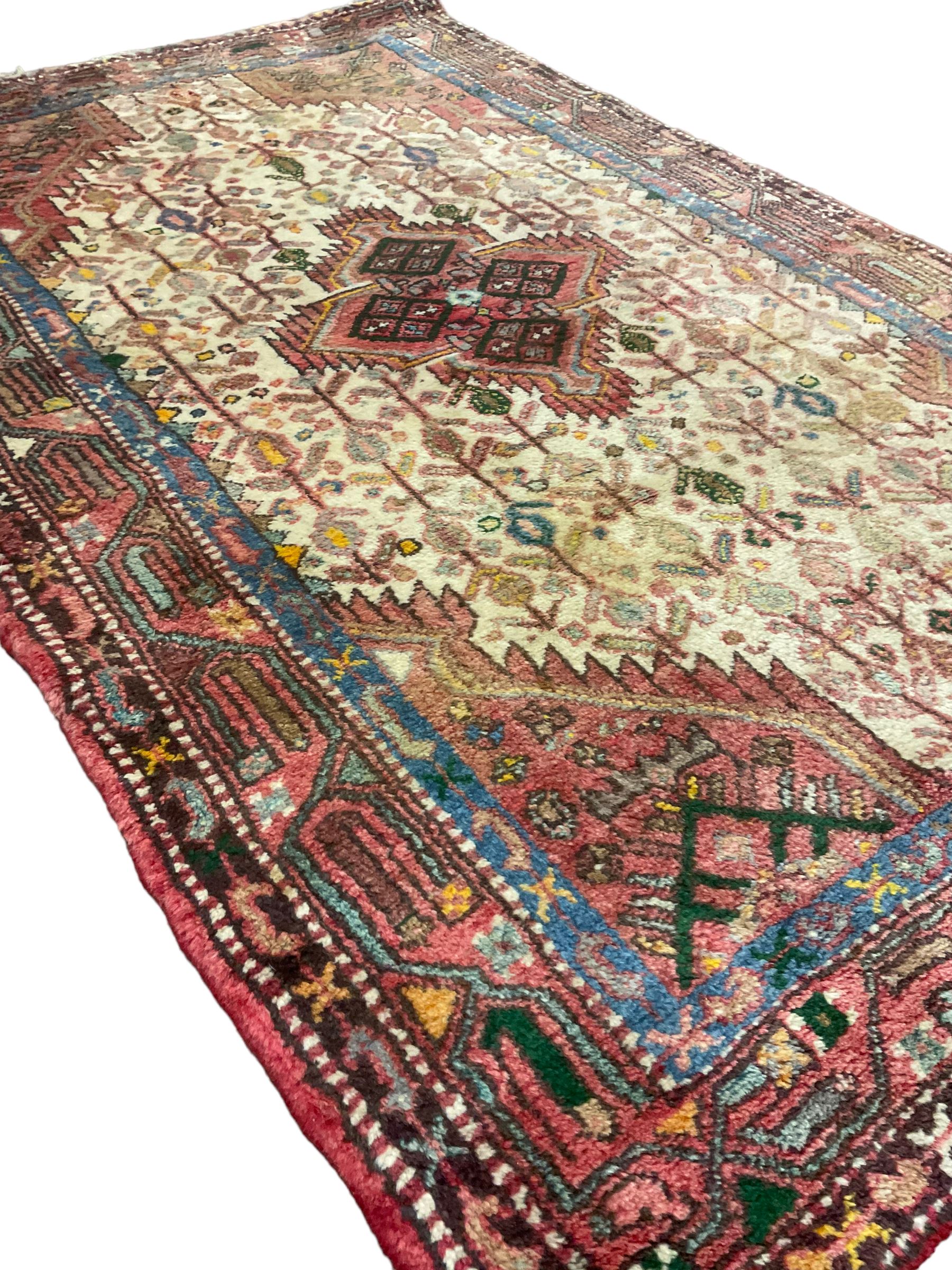 Small Persian rug, ivory and pale red ground, decorated with central medallion within a field of trailing Boteh motifs, geometric design guarded border