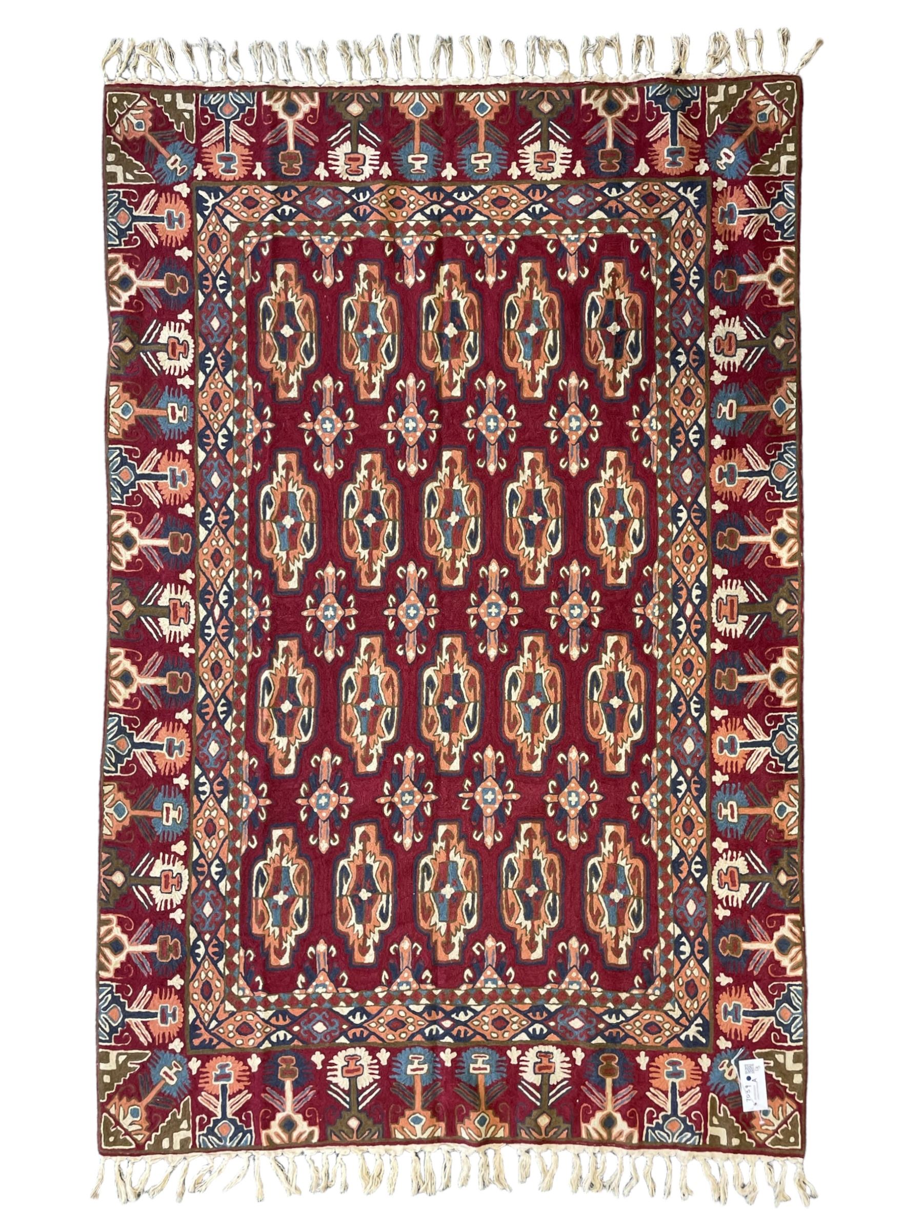 Caucasian design crewelwork hanging, crimson ground, the field decorated with geometric designs, the wide guard band with repeating stylised plant  motifs