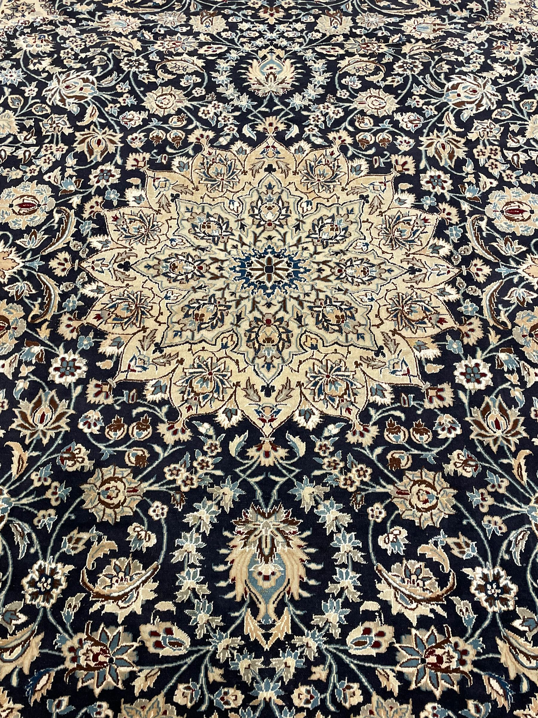 Persian Kashan indigo ground carpet, the central ivory rosette medallion surrounded by trailing and interlaced flower heads and branches, matching spandrels with floral design, the border with scrolling pattern decorated with stylised plant motifs within guards