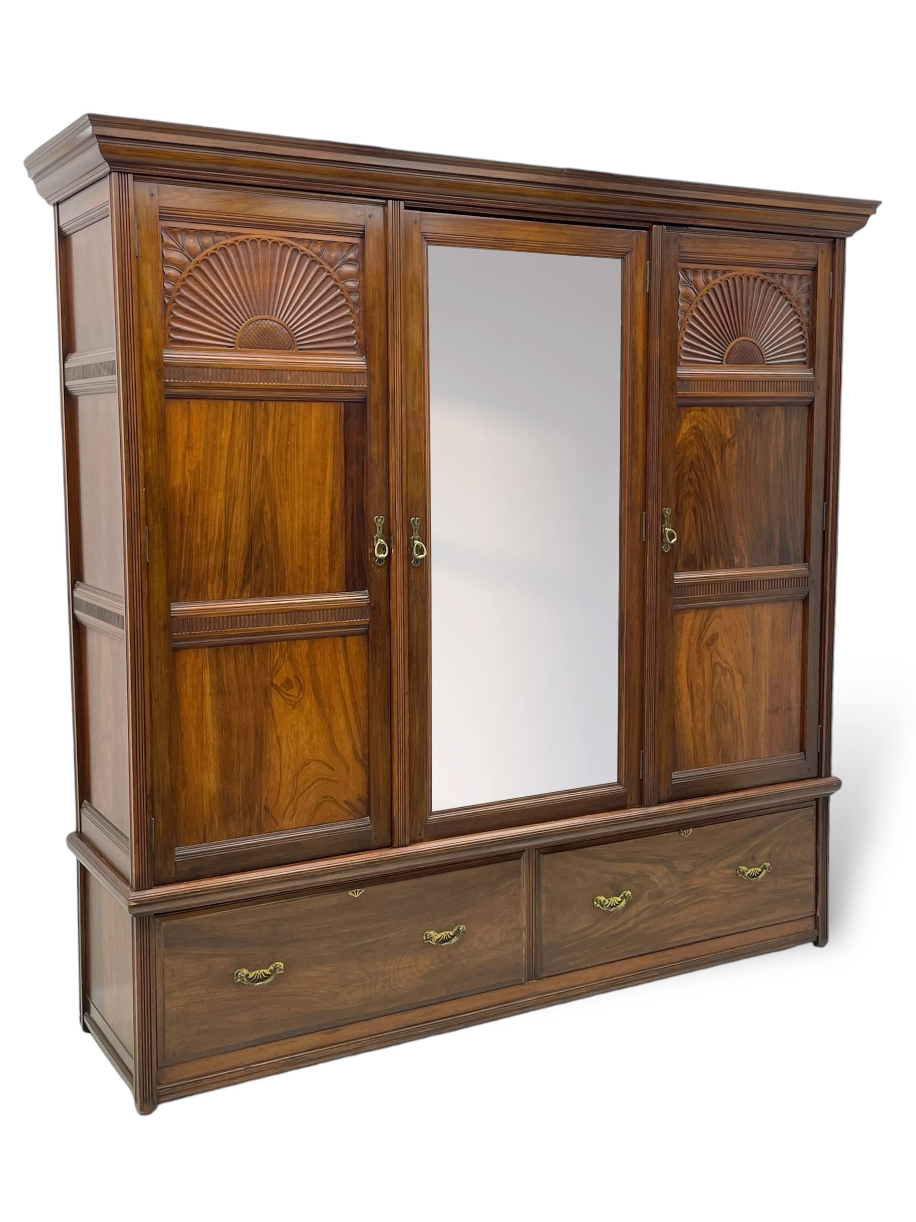 Late Victorian walnut triple wardrobe, projecting moulded cornice over central bevelled mirror door and flanking panelled doors, the top panels carved with fluted fans and stylised leaf motifs, the interior fitted with three linen slides, two drawers and hanging space, two long drawers to base, reed moulded uprights and vertical fluted horizontal rails 