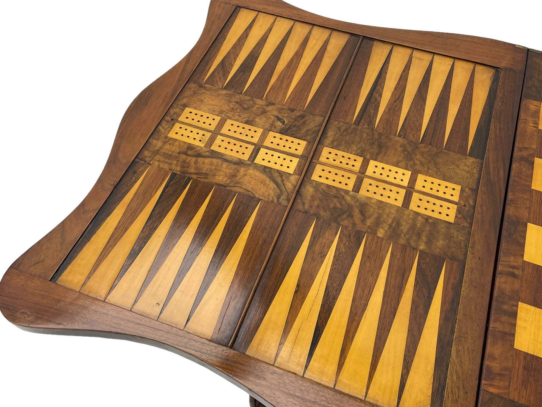 Victorian inlaid figured walnut games table, the serpentine fold-over top inlaid with scrolling foliate decoration, the top opens to reveal cribbage, backgammon and chess boards, single drawer over sliding storage well, on twin pillar supports united by double turned stretchers, on foliage carved out-splayed supports with brass and ceramic castors 