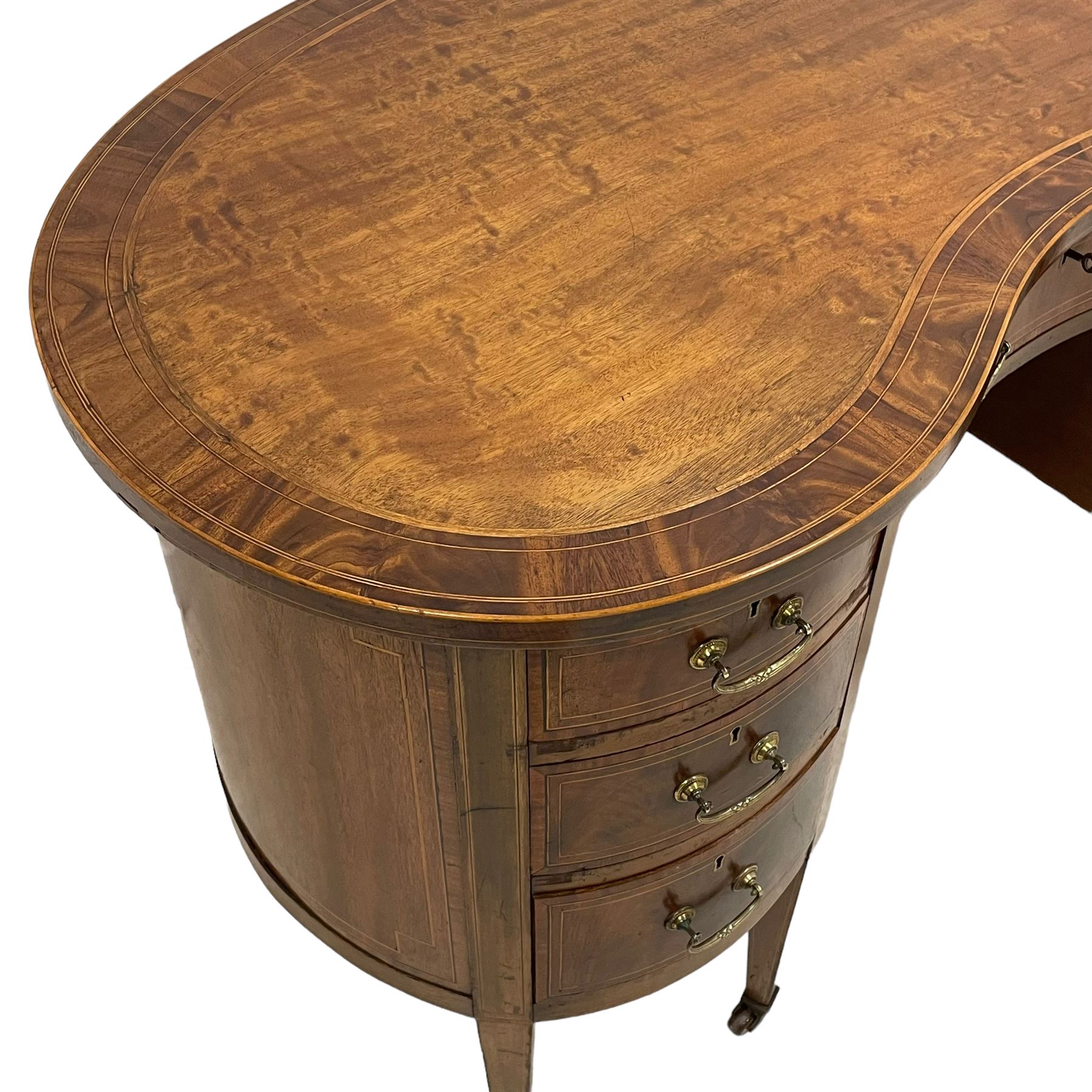 Edwardian mahogany and satinwood banded kidney-shaped writing desk, the shaped top with figured mahogany banding and boxwood stringing, fitted with seven drawers with satinwood bandings, on square tapering supports with brass and ceramic castors