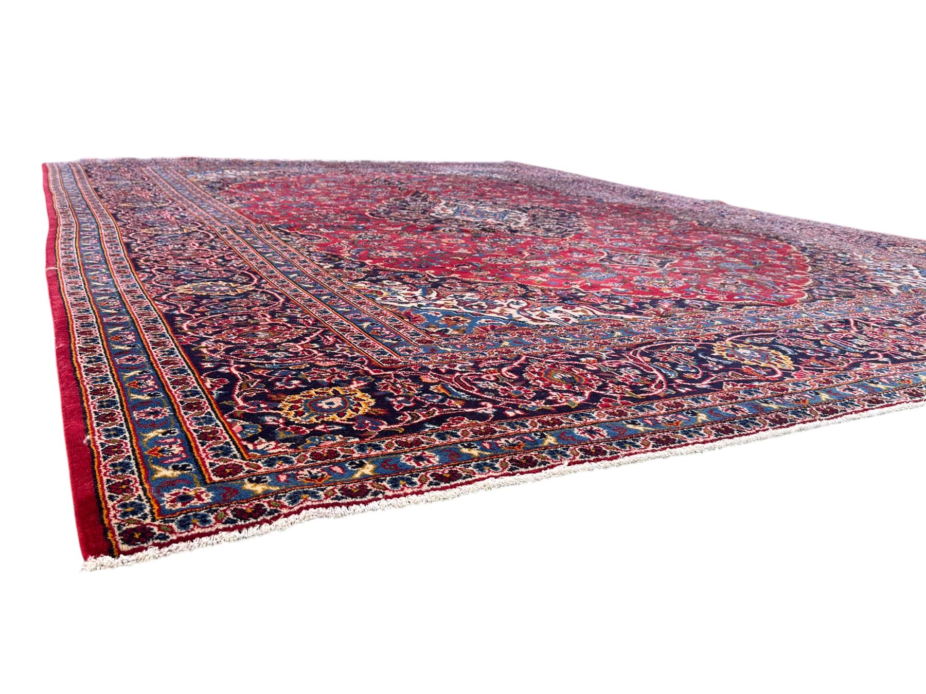 Large Kashan crimson ground carpet, central indigo medallion with stylised floral motifs, flanked by matching spandrels, bordered by multiple bands featuring repeating foliate and floral designs throughout