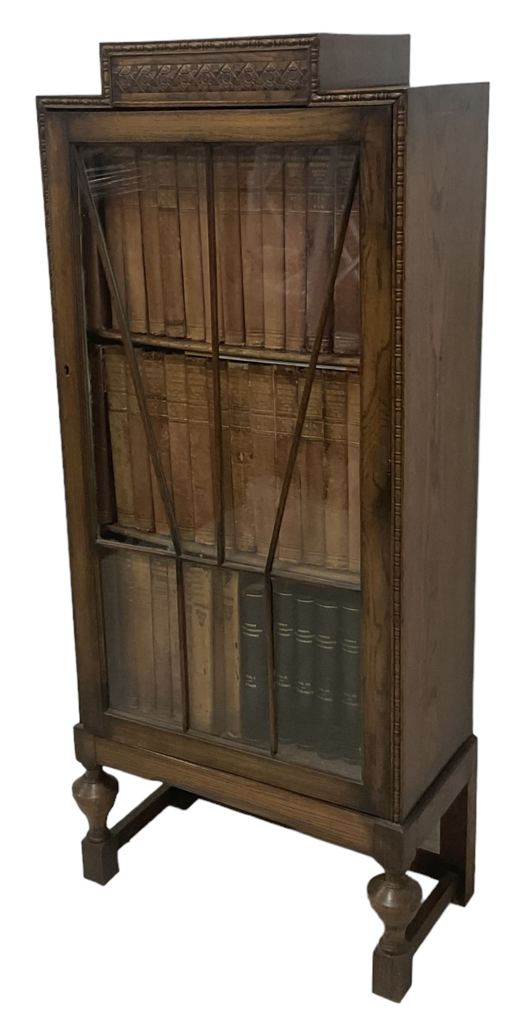 Edwardian oak bookcase, stepped top decorated with beading and stylised floral frieze, single astragal glazed door enclosing encyclopaedias and other books, on turned front feet united by plain stretchers 