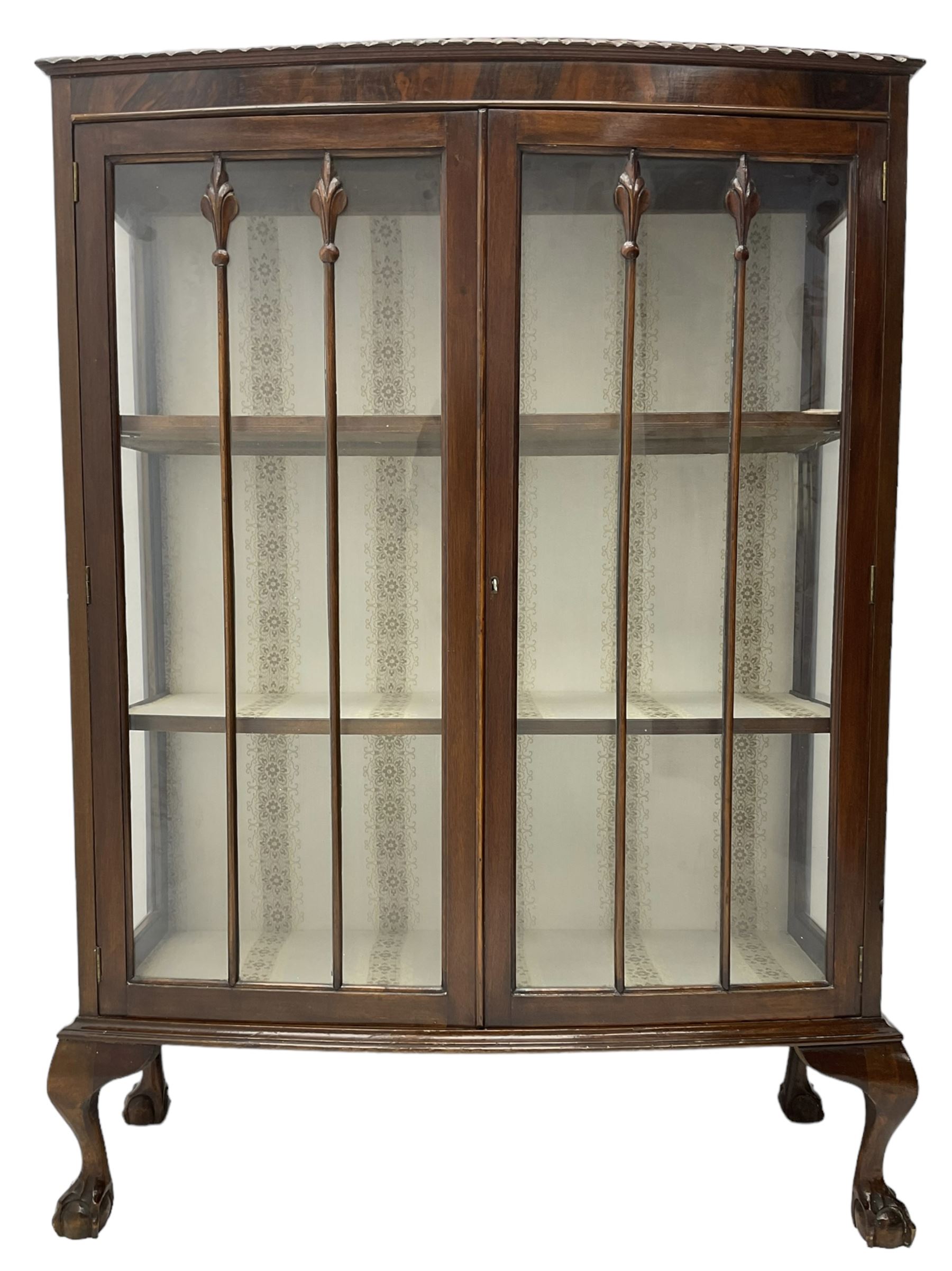 Early 20th century figured walnut bow-front display cabinet, enclosed by two glazed doors, on ball and claw cabriole feet