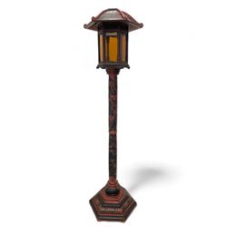 20th century Chinese black and red lacquered hardwood lantern stand, hexagonal shaped canopy top carved with flower heads and scrolls, the lantern fitted with amber tinted glass panes, pierced and carved upper panels, enclosed by two hinged doors, turned stem carved in relief with trailing vine leaves with fruits, stepped hexagonal base with carved decoration  