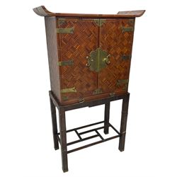 Chinese design bamboo and wood altar cabinet on stand, parquetry lattice-work bamboo, two doors with engraved metal fixtures enclosing drawers and shelf, fitted with slide, the stand pm square supports joined by a series of geometric stretchers