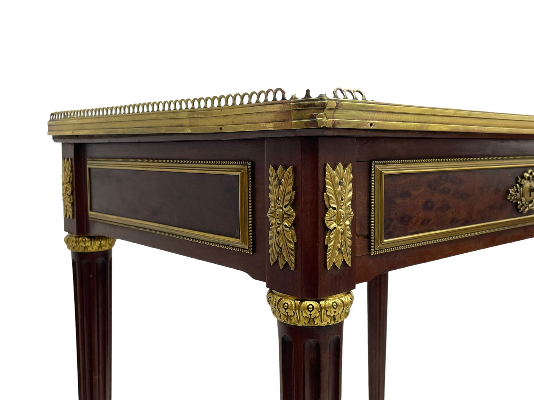 Late 19th century French figured plum pudding mahogany side table, canted rectangular white marble top with raised gilt metal gallery, fitted with a single frieze drawer, central extending floral cast ormolu escutcheon and applied moulded edging, on tapering turned and fluted supports with brass cups and castors, decorated with cast foliate mounts and foliate cast collars 