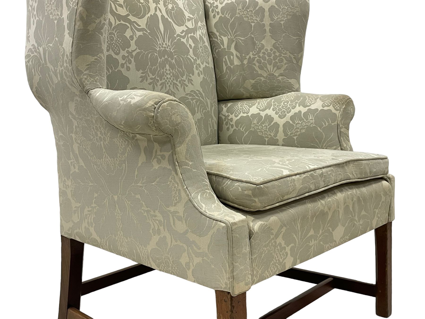 Georgian mahogany framed wingback armchair, upholstered in floral pattern silk damask fabric, wide seat enclosed by rolled arms, on chamfered square supports united by plain stretchers 