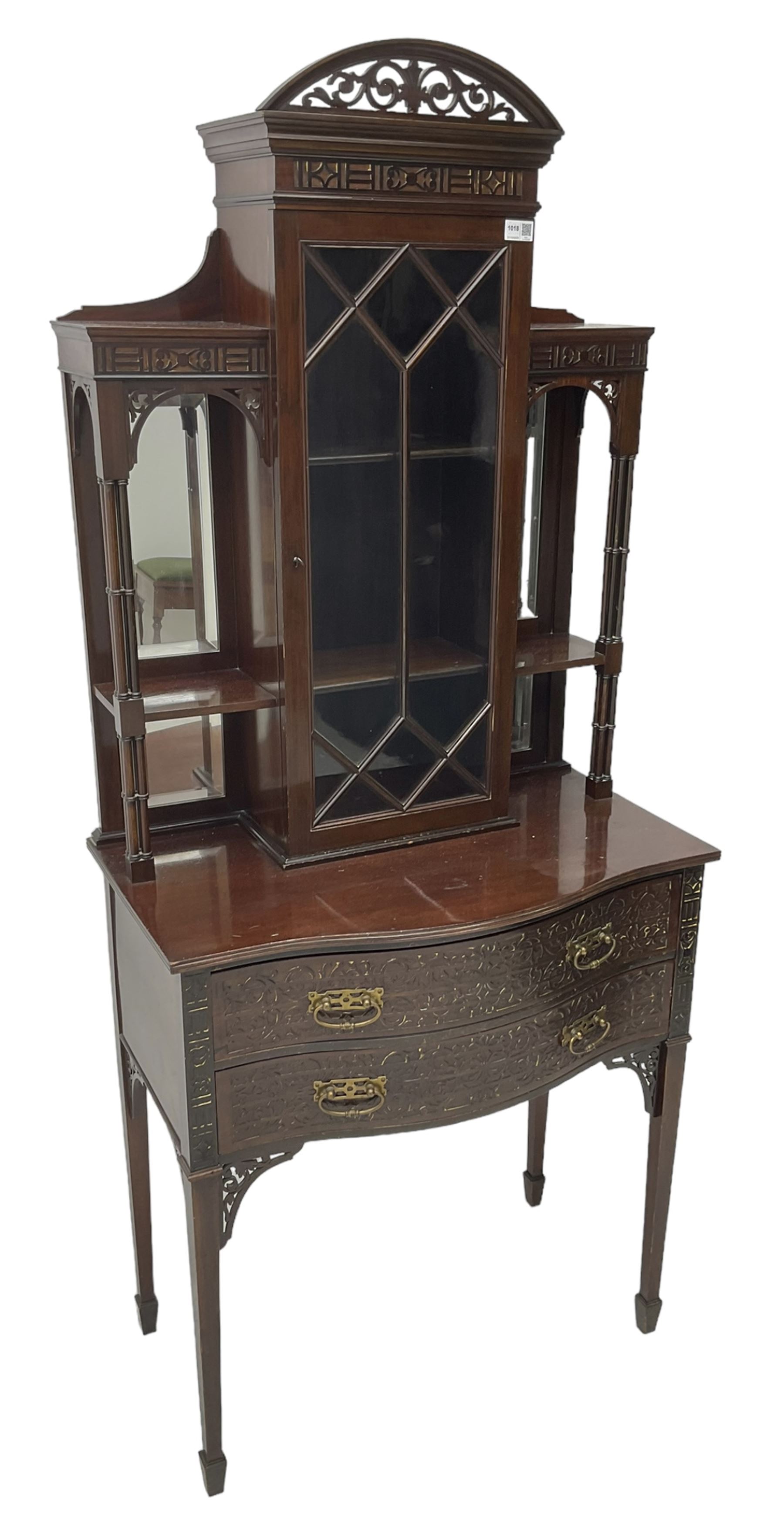 Early 20th century mahogany cabinet on stand, with pierced arched foliate pediment over blind-fretwork frieze, fitted with single astragal glazed door flanked by bevelled mirror back shelves with cluster column uprights, serpentine base fitted with two drawers with blind-fretwork facias 