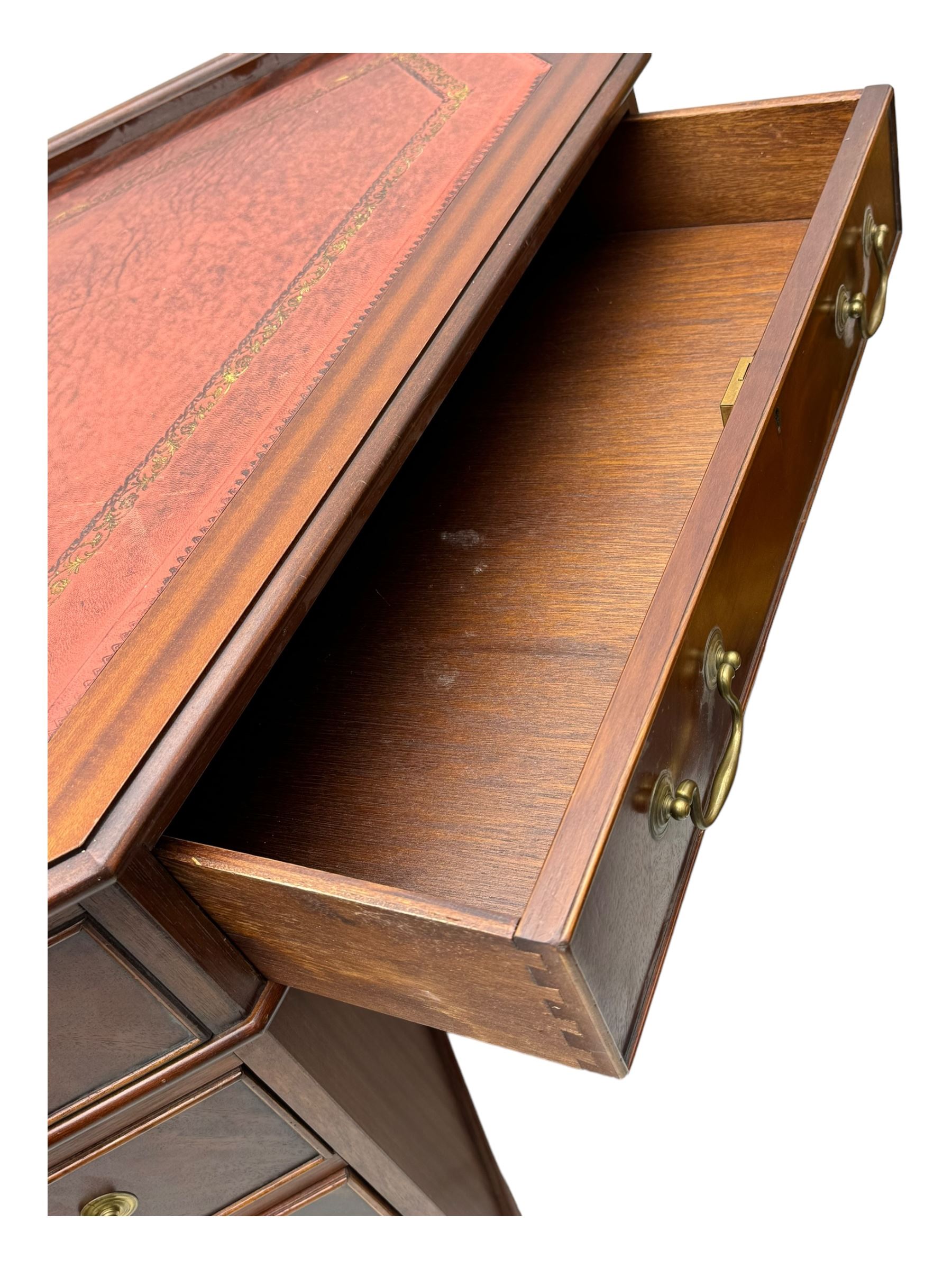 Late 20th century mahogany corner desk, leather inlaid top with gilt tooling, central frieze drawer flanked by two banks of four graduated drawers, raised on shaped bracket supports 