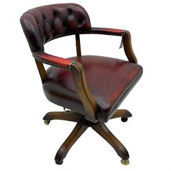 Mid 20th century leather swivel desk chair, oxblood button-tufted upholstery, wooden frame and armrests, on brass castor supports