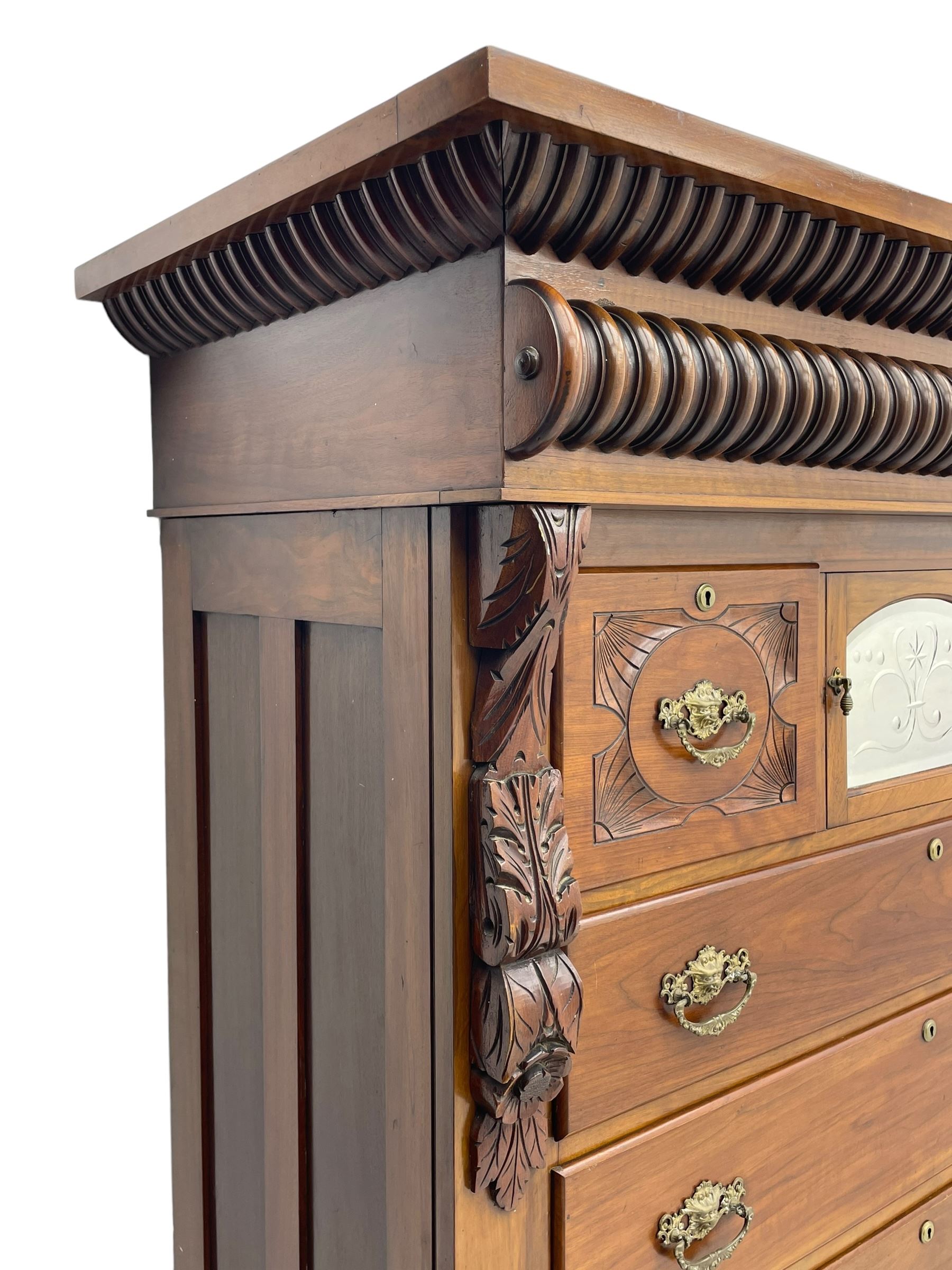 Late Victorian walnut Scotch chest, projecting cornice with turned quarter column mounts over matching half column to frieze, fitted with two upper short drawers with central cupboard, bevelled mirror glazed cupboard door, four graduating drawers below, foliage and flower head carved brackets to the uprights, panelled sides, chamfered plinth on turned feet