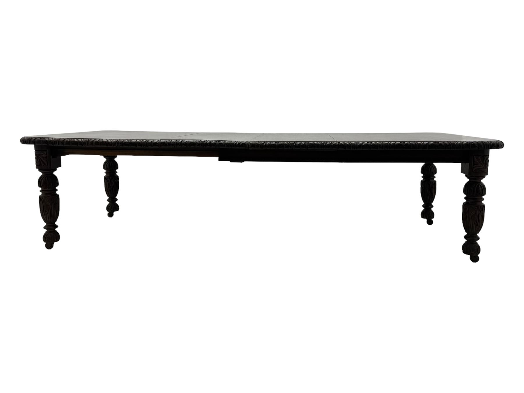 19th century heavily carved oak extending dining table, rectangular top with rounded corners and carved gadrooned edge, extending via winding mechanism with two additional leaves, raised on acanthus leaf-carved baluster supports terminating in ceramic castors