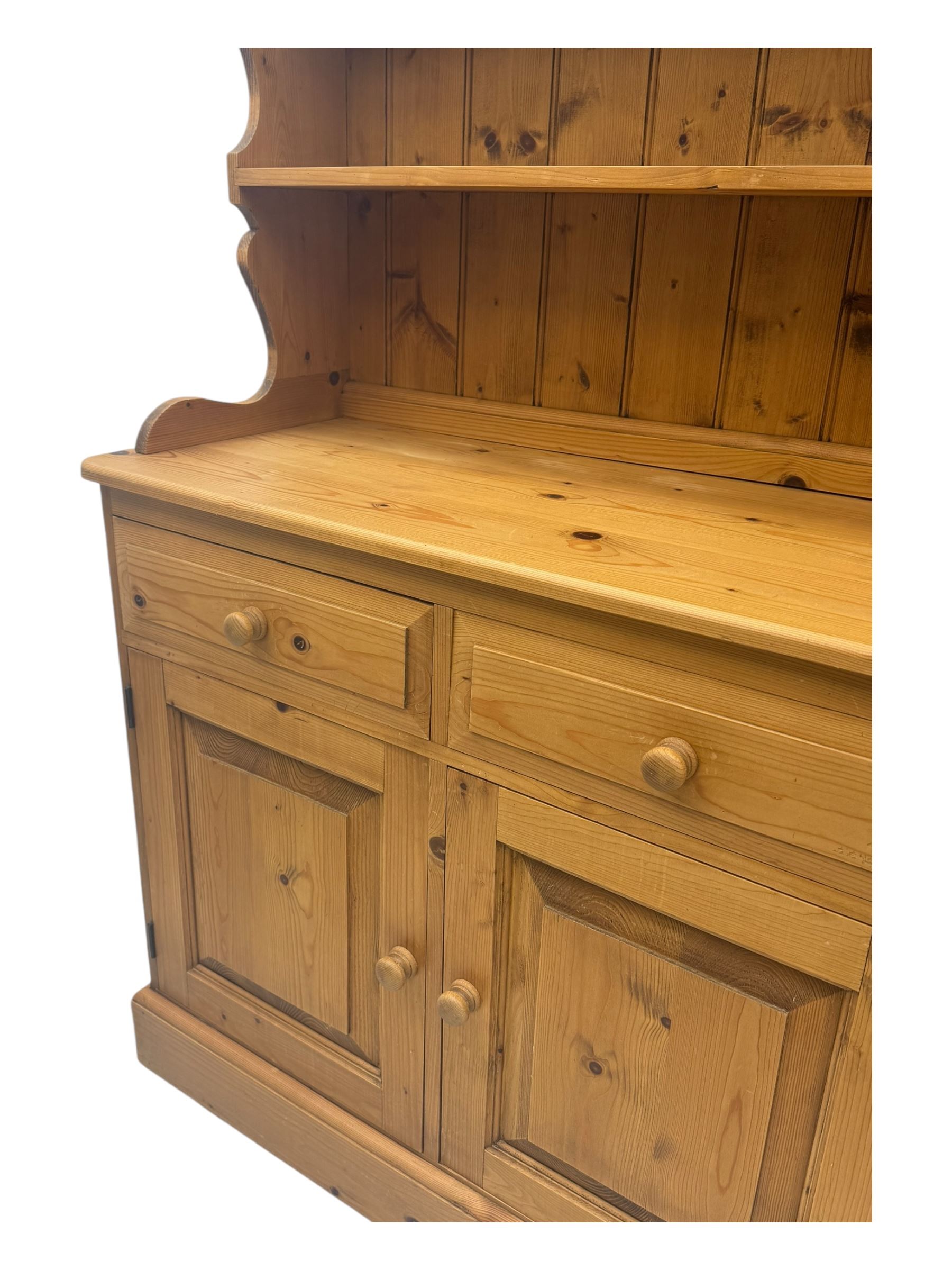 Large traditional pine dresser, shaped cornice over three open shelves, base fitted with four drawers above four panelled cupboards, each with turned wooden knobs, on plinth base