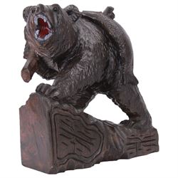 20th century Black Forest carving of a bear carrying a fish upon its back, with open mouth, painted tongue and teeth, and inset glass eyes, stood  upon a naturalistic base, overall H37cm L34cm W18cm