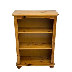 Traditional pine open bookcase, featuring arched top section flanked by fluted side supports, two adjustable shelves and cast iron coat hook with cat motif to the left side, standing on round bun feet 