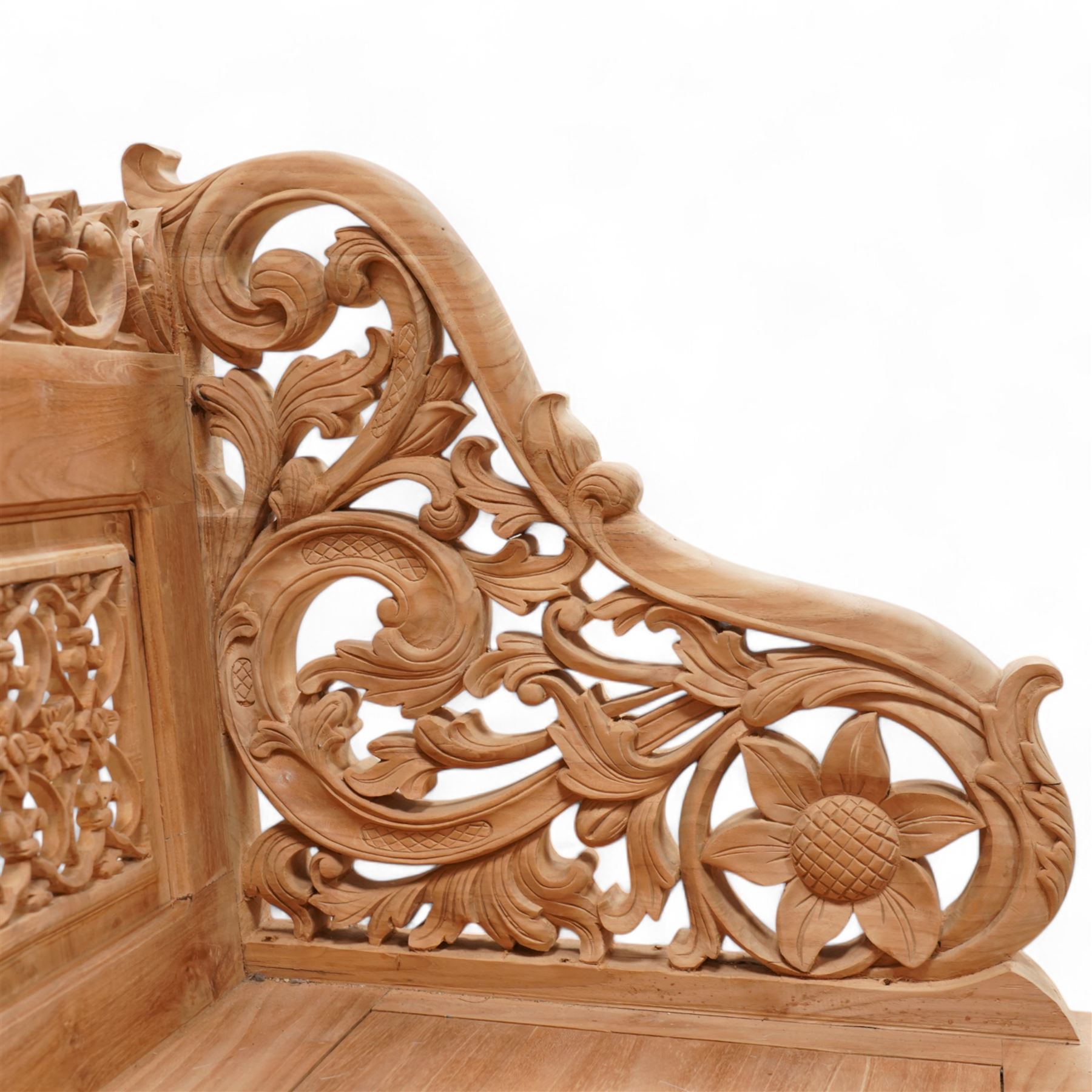 Hand carved teak garden bench, C-scroll and foliate carved cresting rail over four pierced and flower head carved panels, shaped and scrolling end supports carved with flower heads and curling leafy branches, united by pegged stretcher