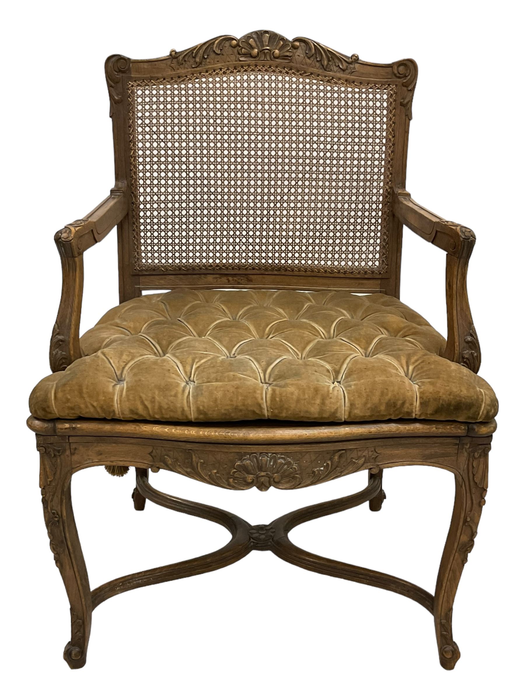 Late 19th century French carved beech open elbow chair, shaped cresting rail carved with central shell and curl leafage, cane work seat and back with buttoned loose seat cushion, the open arms carved with scrolled terminals and acanthus leaves, on cabriole supports with carved decorated united by shaped and moulded x-framed stretchers 