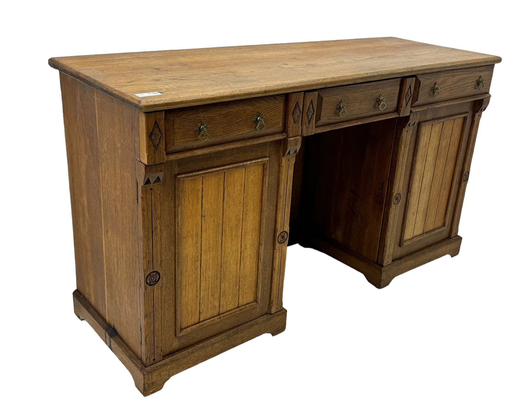 Late Victorian oak twin pedestal desk, chamfered rectangular top over three convex front edge drawers and two panelled cupboards, flanked by carved supports with roundels and diamond motif, on bracketed plinth base