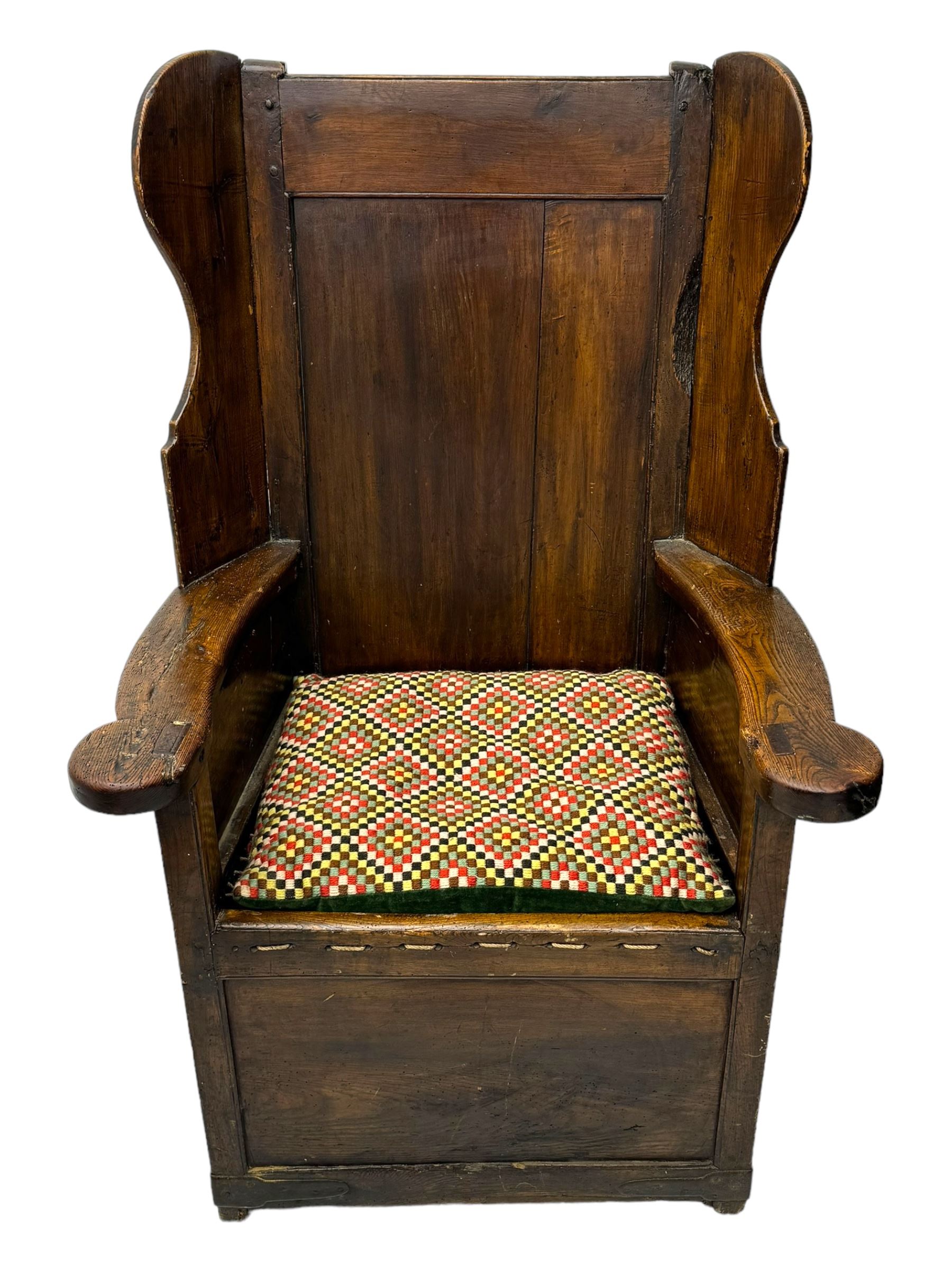 George III oak lambing chair, tall rectangular panelled backrest with shaped wings over broad scrolled armrests, box seat with removable geometric upholstered cushion, integrated drawer to lower section, resting on square supports