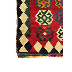 Southwest Persian Qashqai Kilim red ground rug, the central field adorned with rows of multicolored hexagonal medallions with geometric patterns, the border featuring alternating black and white stepped diamonds, narrow band to one end decorated with multicoloured geometric figures