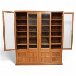 Eagleman - oak bookcase, penny moulded cresting rail over four glazed doors and four panelled doors, fitted with adjustable shelves, on moulded plinth base, panelled sides, carved with eagle signature, by Albert Jeffray, Sessay, Thirsk