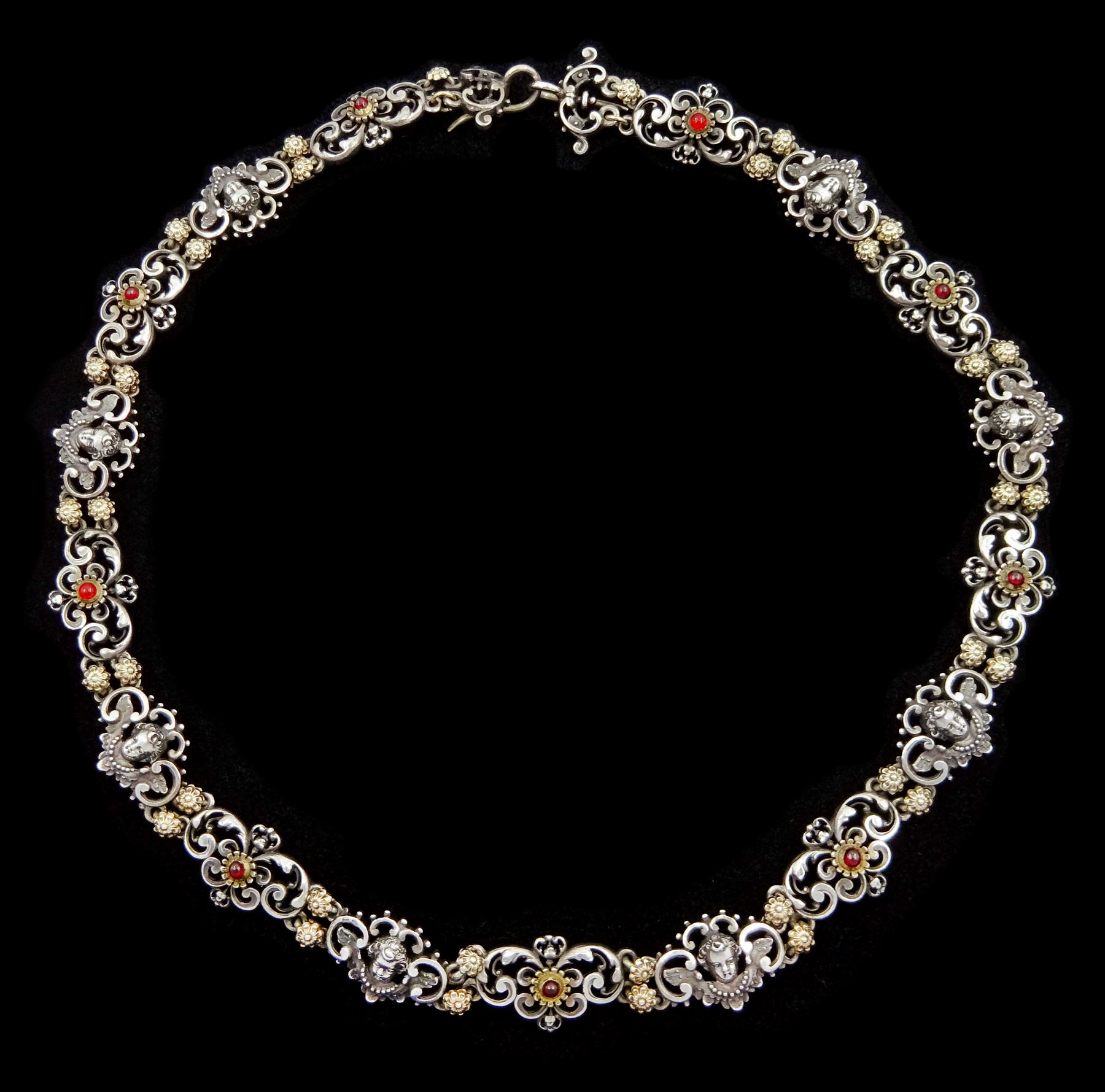 Early 20th century continental silver scroll link necklace, alternate panels of winged cherub and silver-gilt cabochon red paste stones, separated by silver-gilt flower head links, indistinct hallmarks, possibly Austrian or German