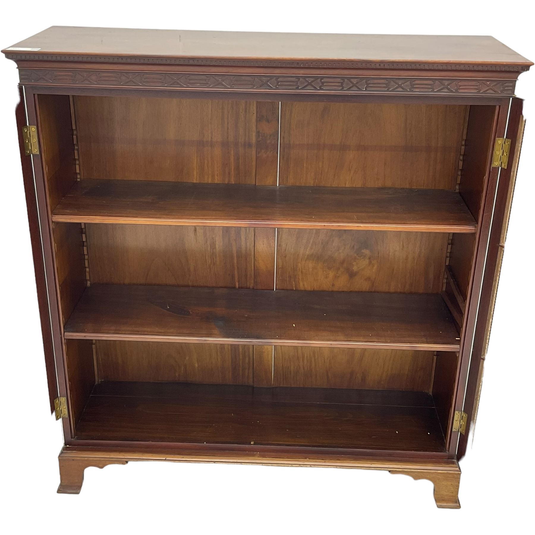 Early 20th century mahogany bookcase, projecting dentil cornice over blind fretwork frieze, enclosed by two astragal glazed doors, on shaped bracket feet 