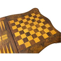 Victorian inlaid figured walnut games table, the serpentine fold-over top inlaid with scrolling foliate decoration, the top opens to reveal cribbage, backgammon and chess boards, single drawer over sliding storage well, on twin pillar supports united by double turned stretchers, on foliage carved out-splayed supports with brass and ceramic castors 