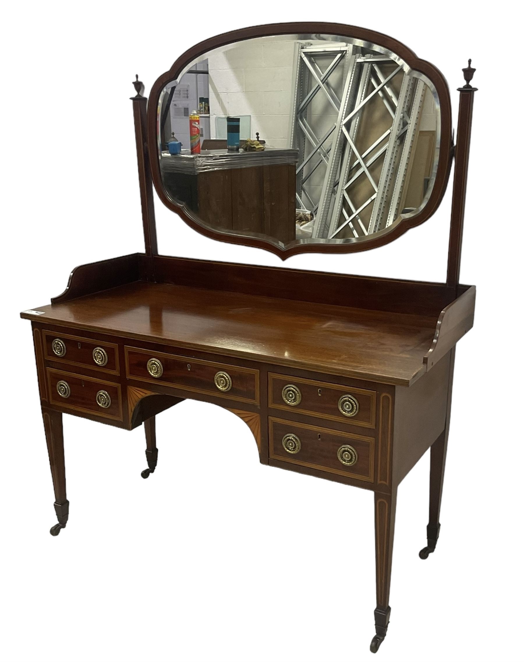 Edwardian inlaid mahogany kneehole dressing table, raised shaped oval bevelled mirror back, fitted with five drawers with banding and stringing, on square tapering supports with castors